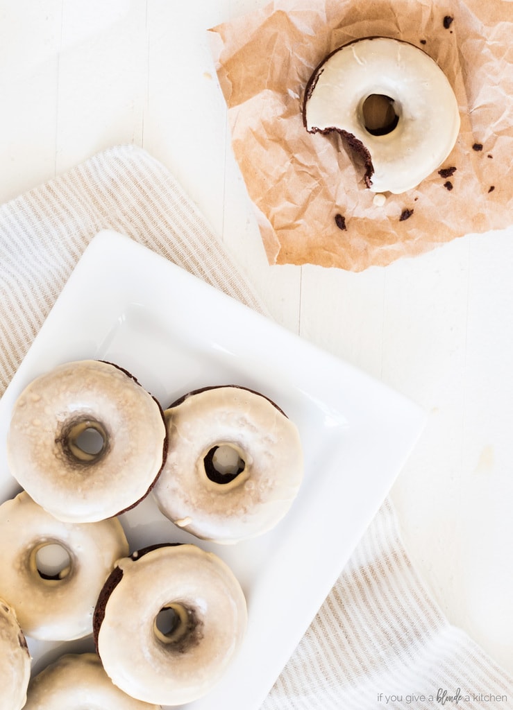 guinness chocolate donuts on plate with izing. Donut with bite removed and crumbs on brown baking paper. White wood background