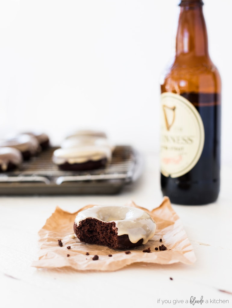 guinness chocolate donuts with stout beer bottle. Donut with a bite on brown baking paper . Donuts on wire cooling rack in the background with glaze