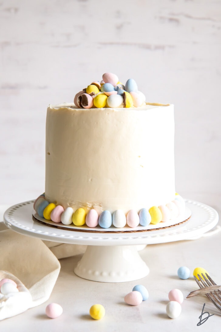 white cake stand holding a cadbury mini egg cake with buttercream frosting and pastel easter egg candies for garnish
