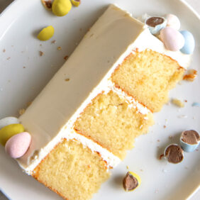 slice of triple layer cadbury mini egg cake with vanilla frosting on a plate with broken chocolate mini eggs