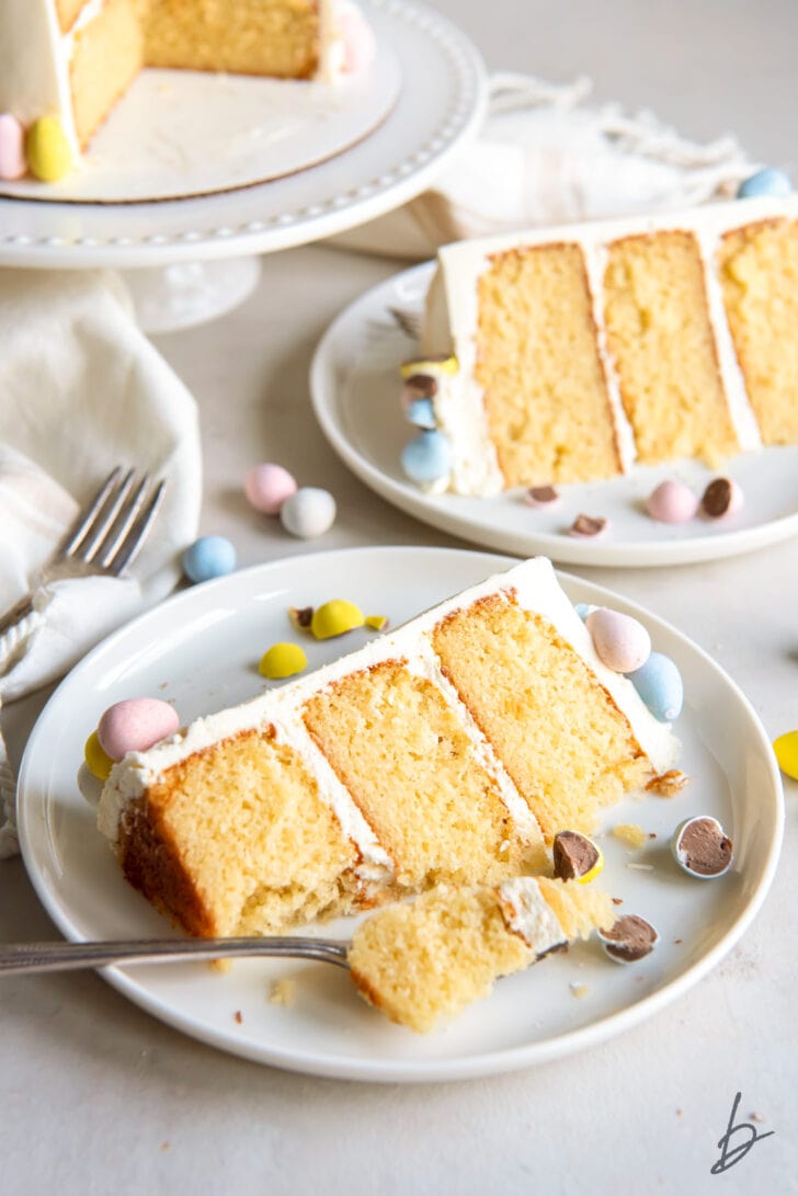 triple layer cadbury mini egg cake slice on plate with fork taking bite and another plate with cake slice behind it