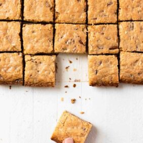 Pecan coconut blondies cut into squares with hand taking one from the symmetrical bars