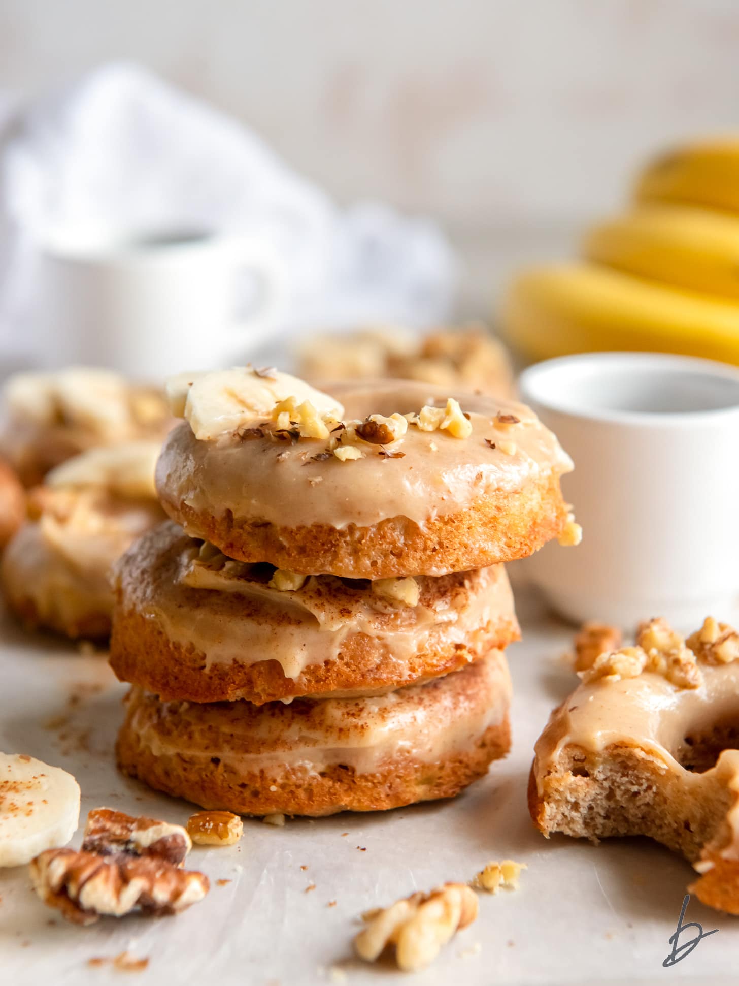 stack of three banana donuts with brown butter glaze and walnuts as garnish.