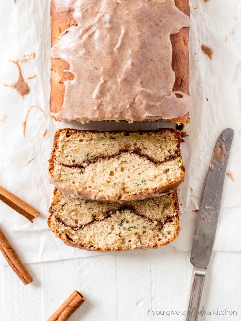 cinnamon swirl zucchini cake cut with slices showing cinnamon swirl. Knife with icing and cinnamon sticks