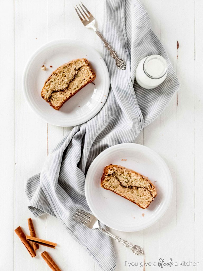 cinnamon swirl zucchini cake slices on white plates with forks and striped kitchen towel. White wood background, milk bottle and cinnamon sticks