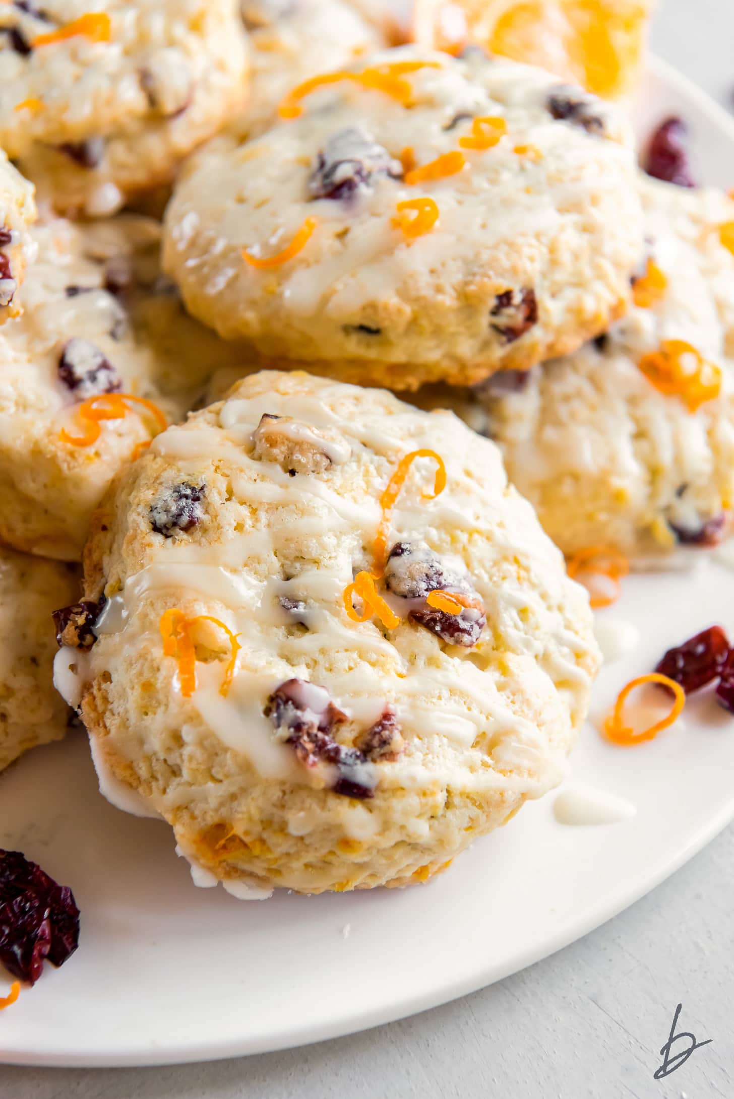 cranberry orange scone with glaze leaning up against more scones on a plate.