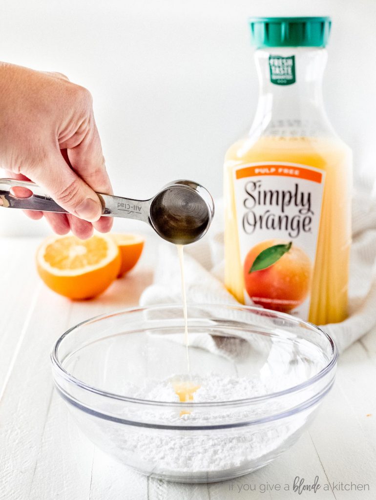 handholding tablespoon pouring orange juice into bowl