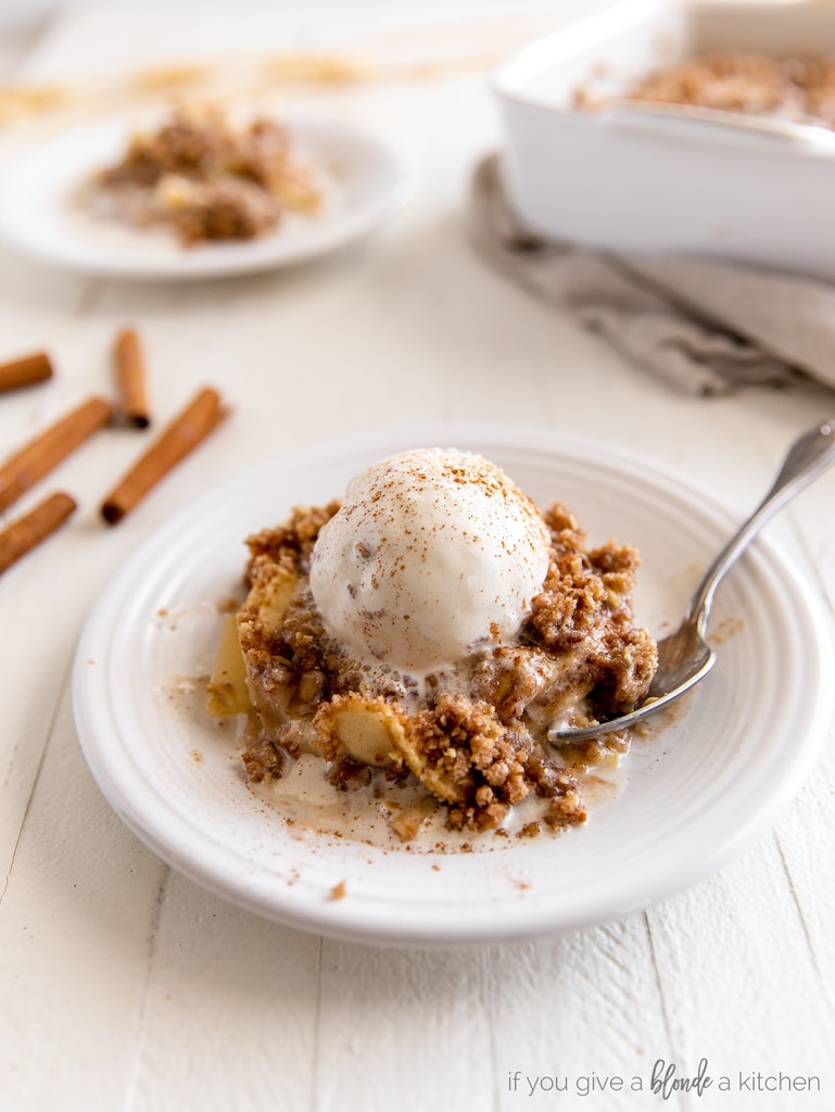 Serving of apple crisp with scoop of vanilla ice cream on white round plate.