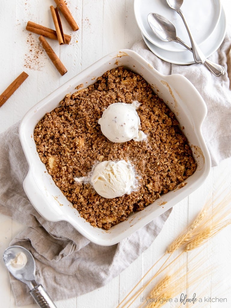 Apple crisp in square ceramic baking dish with two scoops of vanilla ice cream on top.