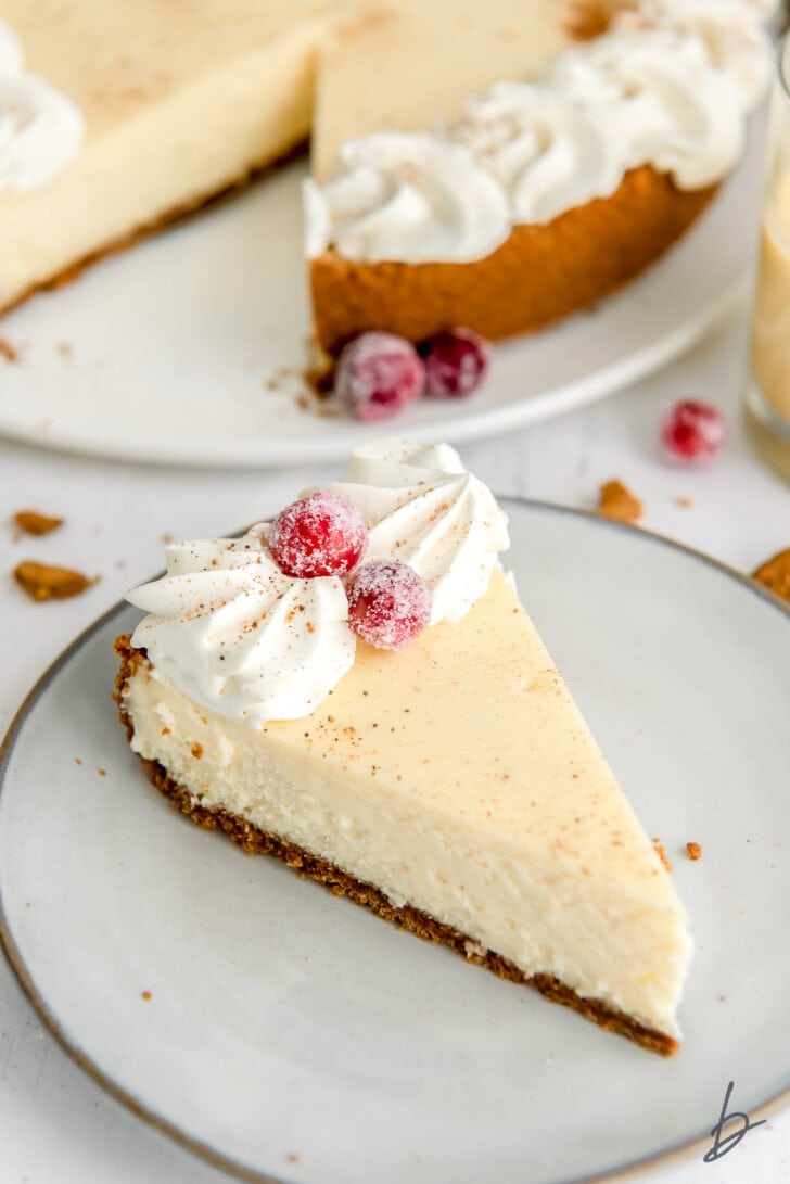 slice of eggnog cheesecake with gingersnap crust, whipped cream and sugared cranberries
