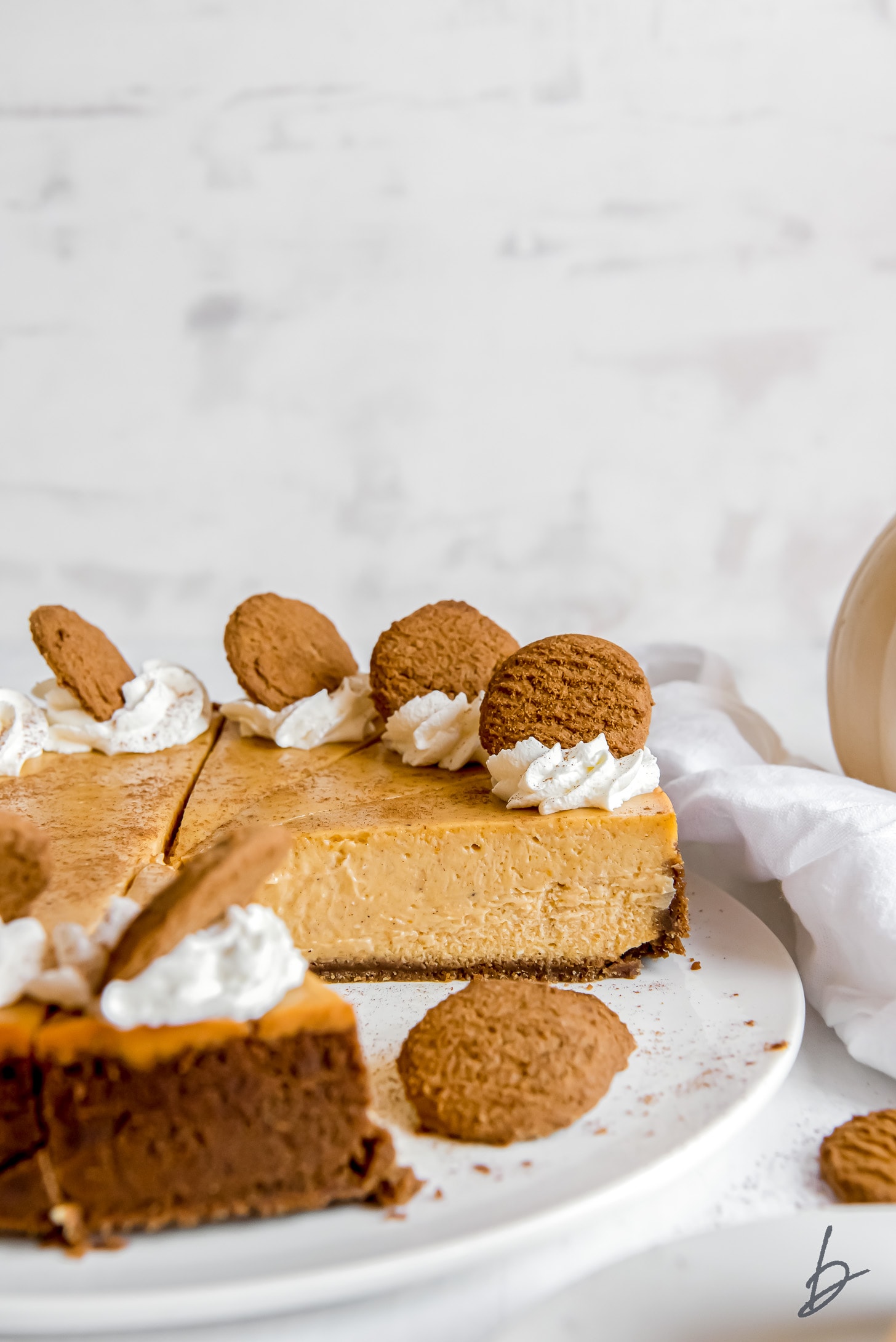 Side of pumpkin cheesecake with gingersnap crust garnished with whipped cream and gingersnap cookie.