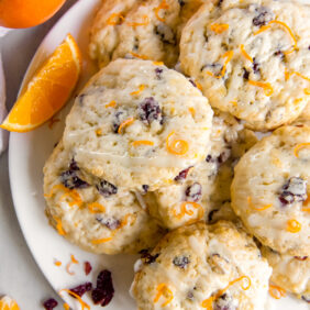 glazed cranberry orange scones on a plate with orange zest and dried cranberries.
