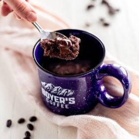 hand holding spoon with double chocolate chip cookie. Blue mug with cookie inside