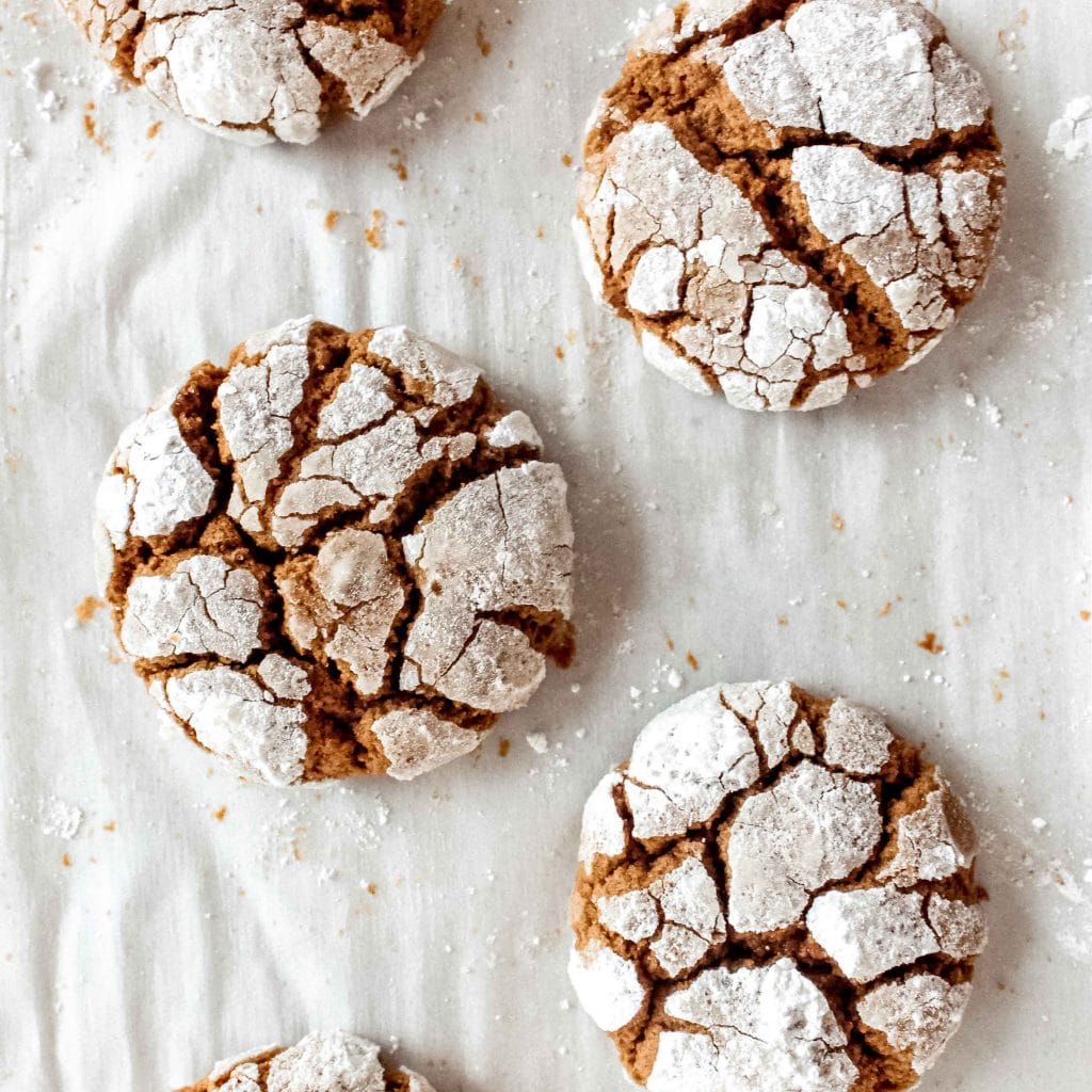 gingerbread crinkle cookies covered in powdered sugar on white parchment paper