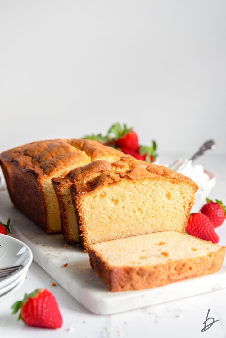 loaf of cream cheese pound cake with three slices cut off end next to fresh strawberries