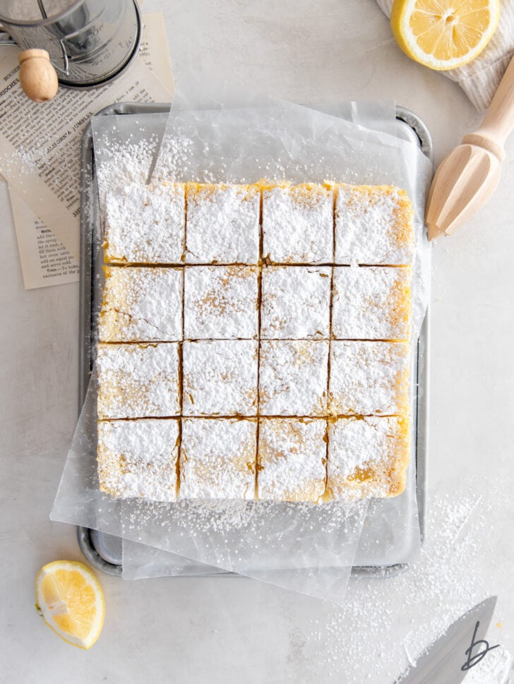 powdered sugar dusted lemon bars cut into squares on wax paper on baking sheet