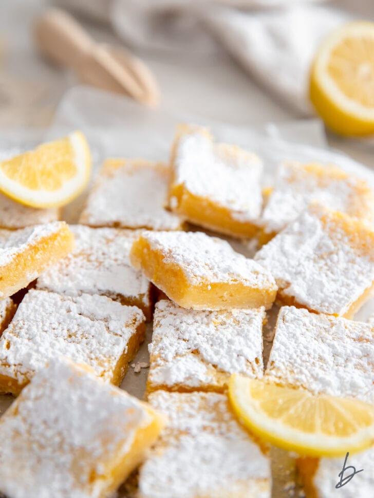 pile of lemon bars with confectioners sugar and one lemon bar on its edge showing gooey filling