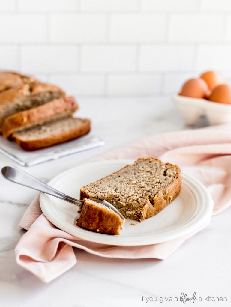 slice of banana bread on white plate with fork taking bite