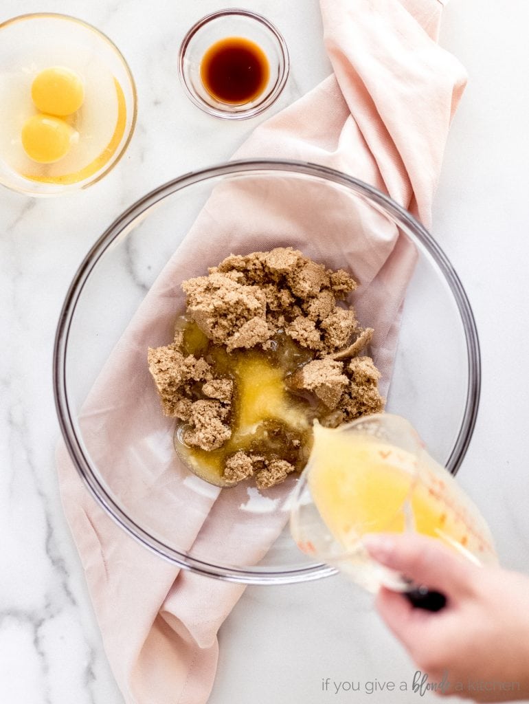 hand pouring melted butter on top of brown sugar in mixing bowl