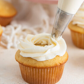 vanilla buttercream frosting being piped on top of a vanilla cupcake.