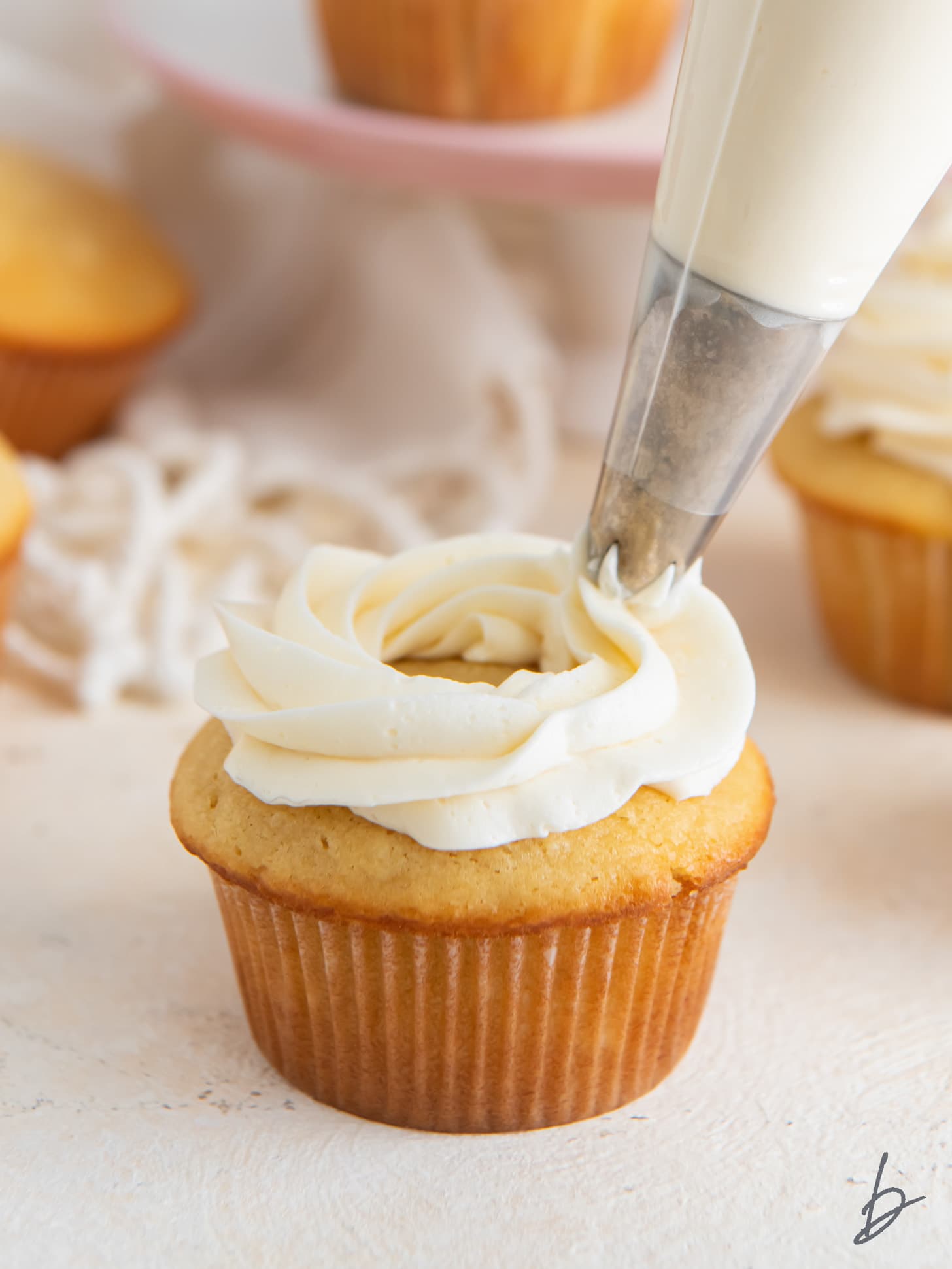 vanilla buttercream frosting being piped on top of a vanilla cupcake.