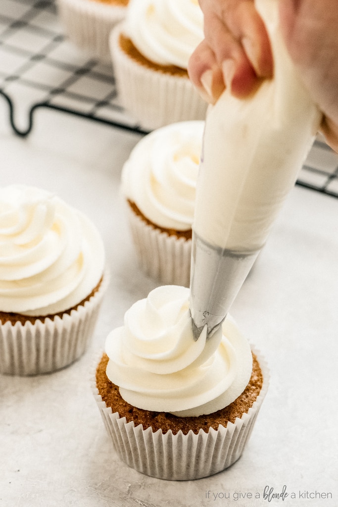 frosting bag piping cream cheese frosting on carrot cake cupcake