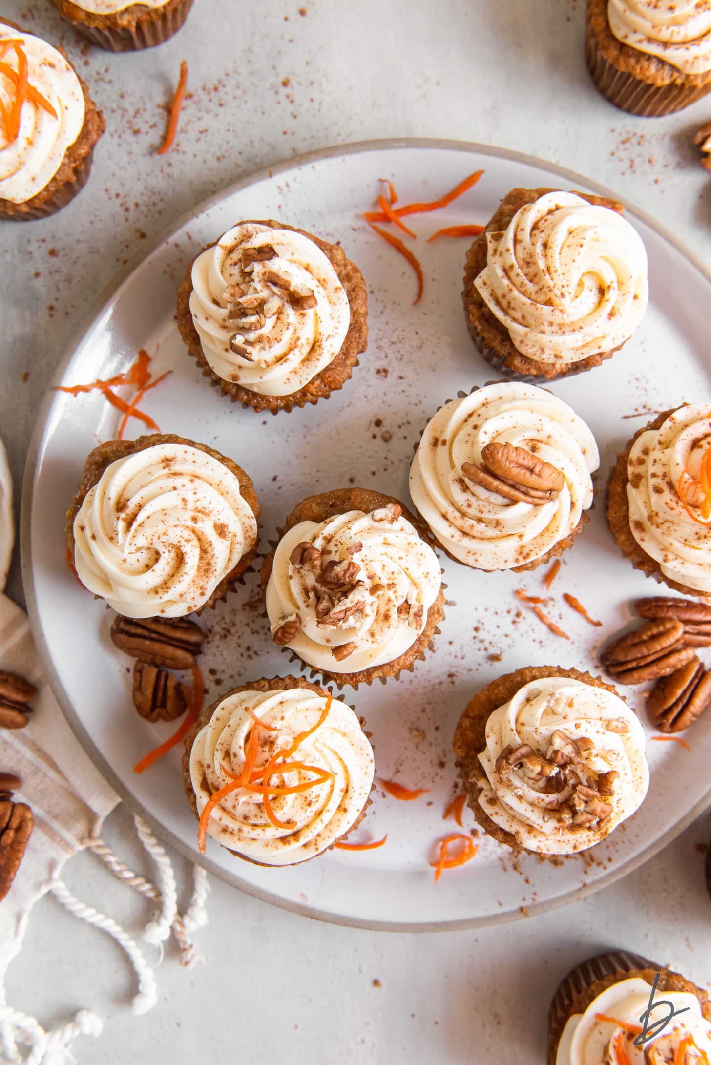 shredded carrot, chopped nuts and cream cheese frosting on top of cupcakes on a plate.