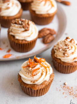 carrot cake cupcakes with cream cheese frosting and chopped nuts on top.