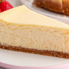 slice of homemade cheesecake with graham cracker crust on a round plate