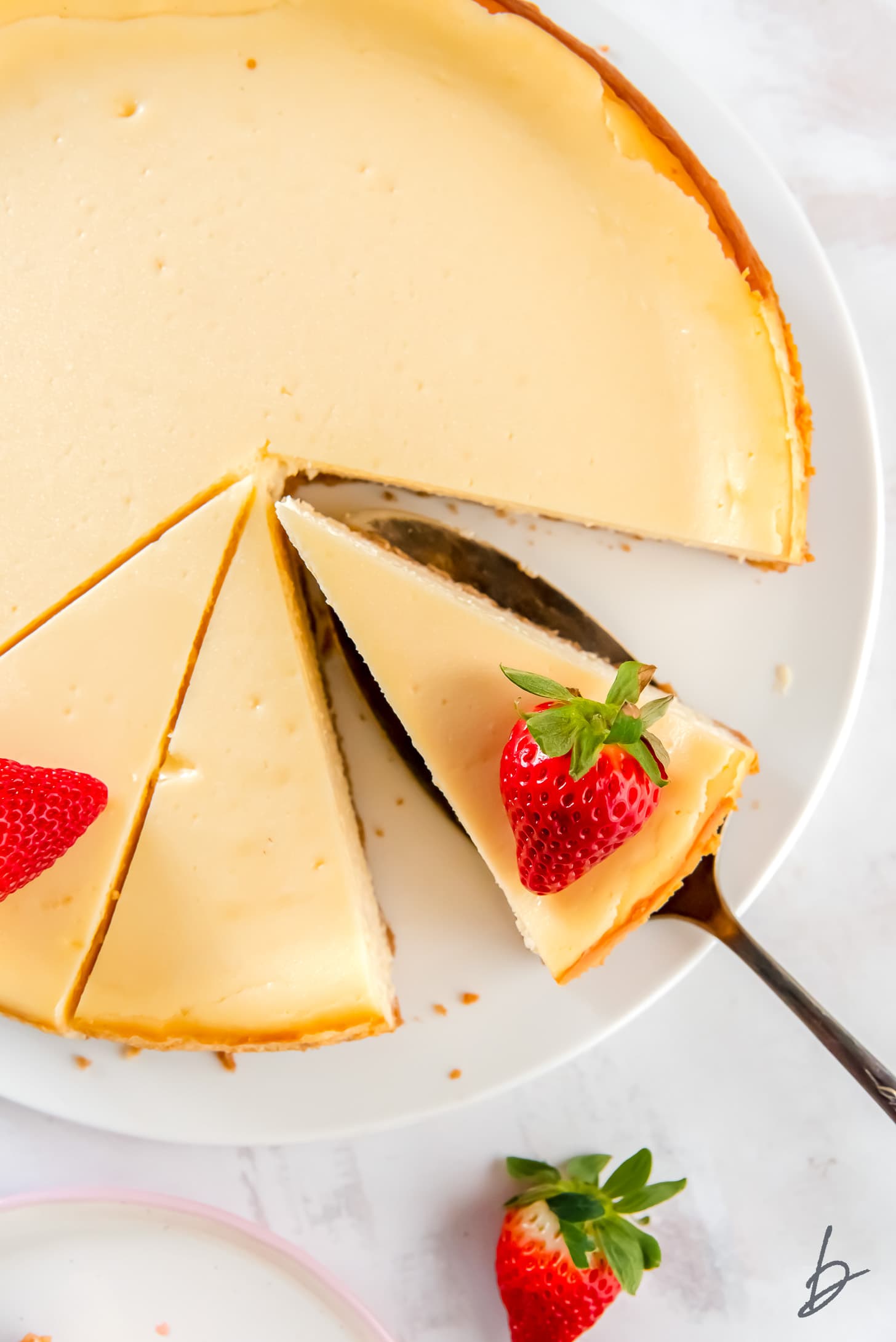 cake plate with whole cheesecake and cake server holding cheesecake slice with strawberry garnish