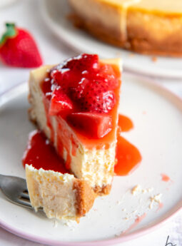 cheesecake slice on plate with strawberry sauce and fork taking bite