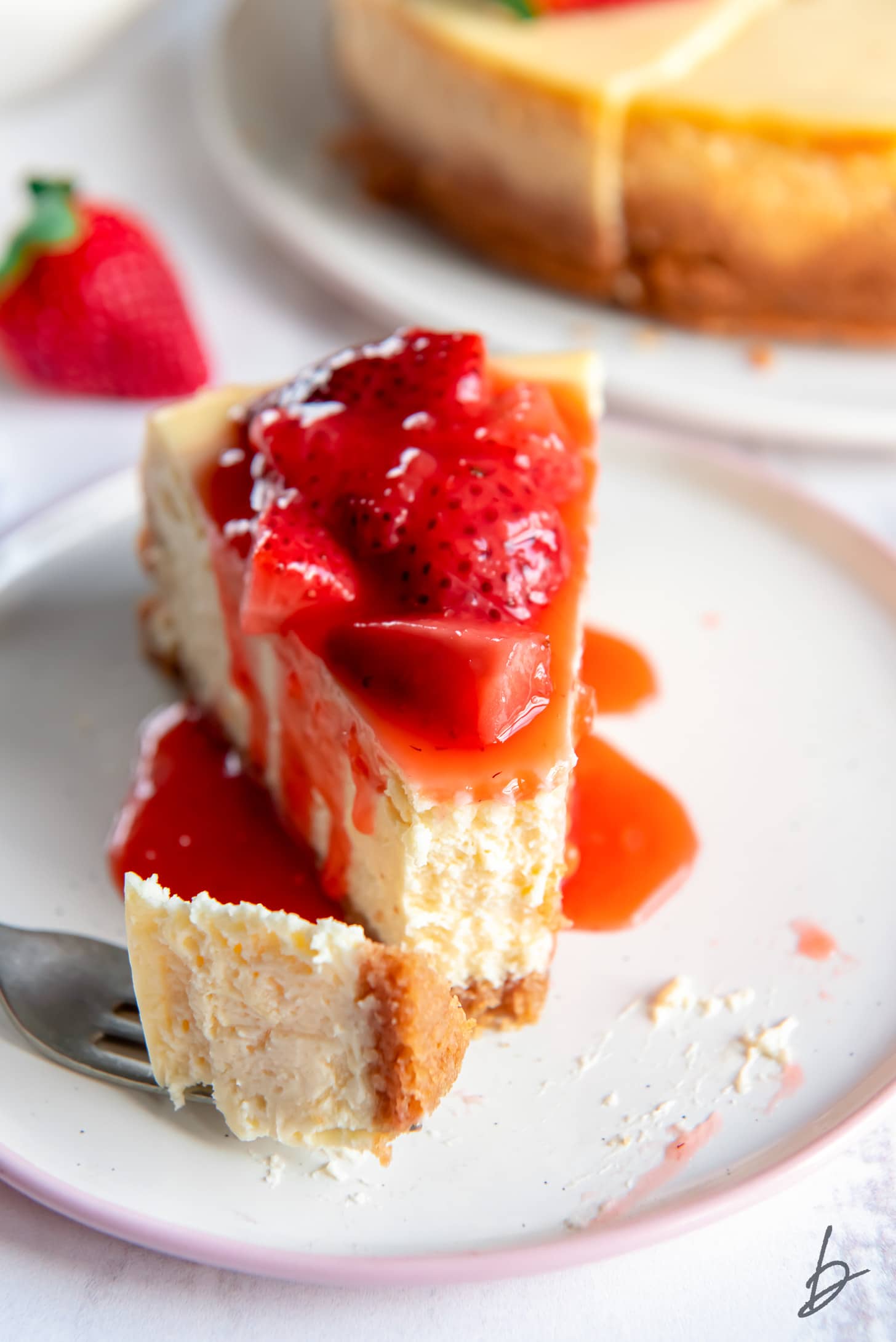 cheesecake slice on plate with strawberry sauce and fork taking bite
