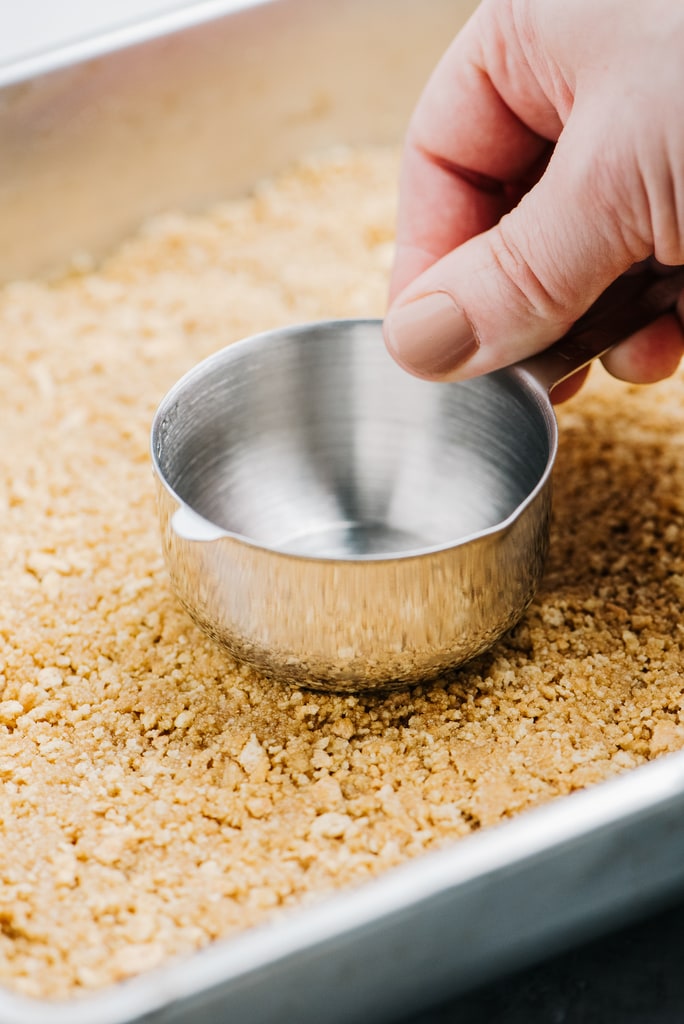 measuring cup press crushed graham crackers into baking pan