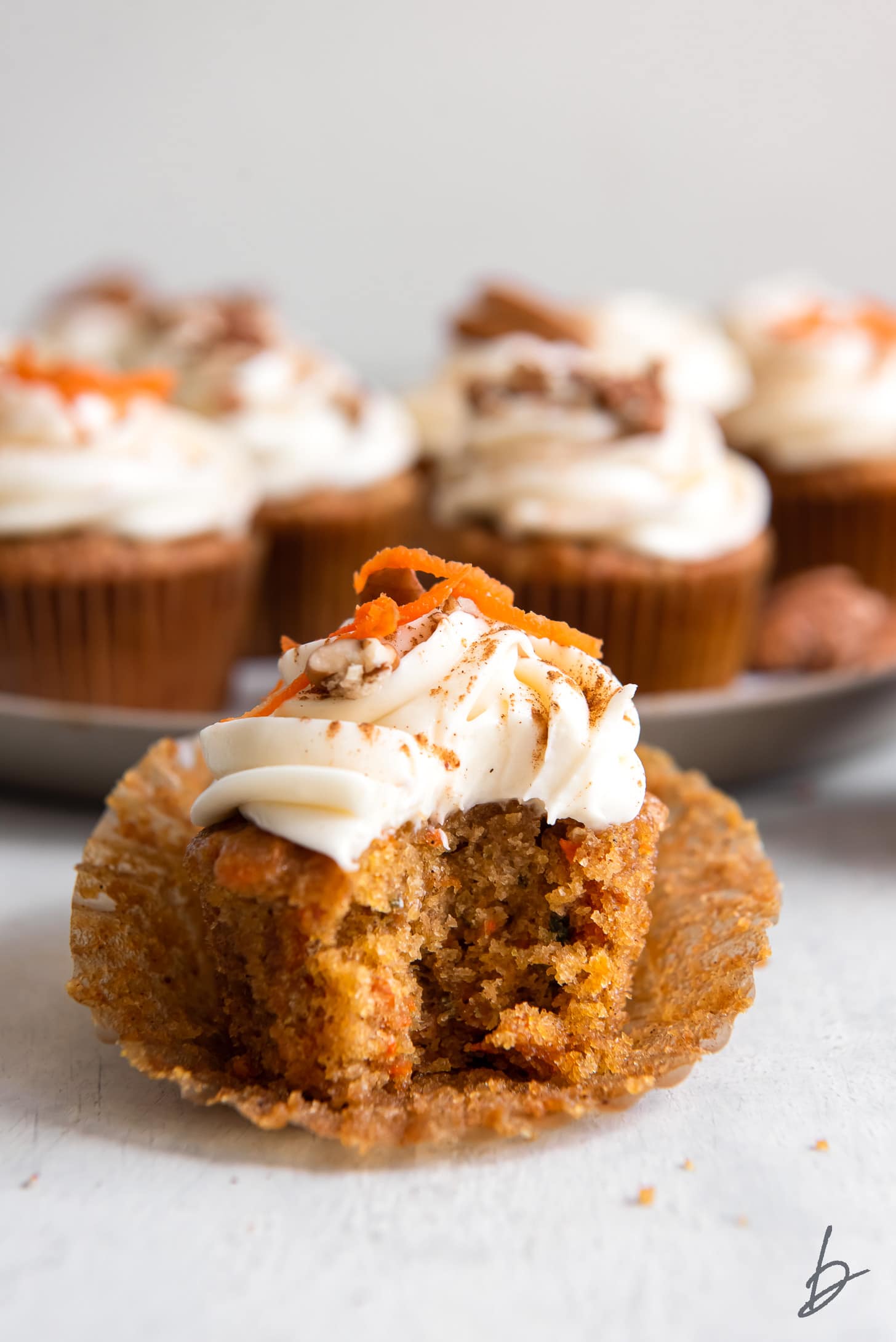 carrot cake cupcake with a bite on a paper cupcake liner.