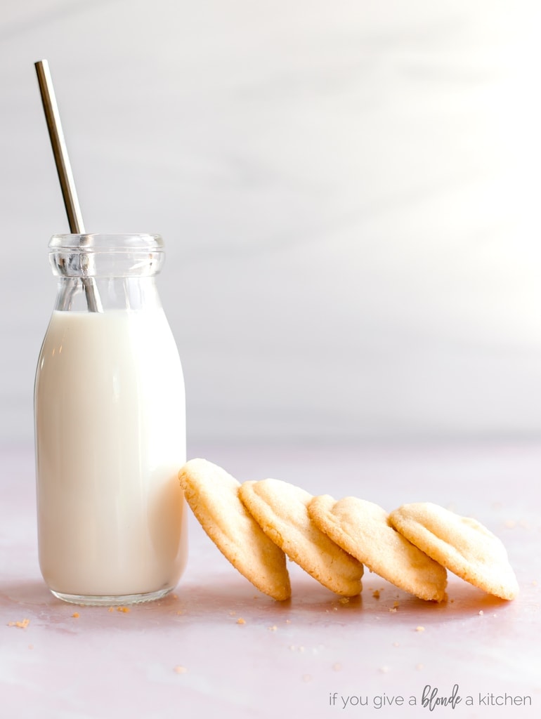 four sugar cookies stacked against glass bottle of milk with metal straw