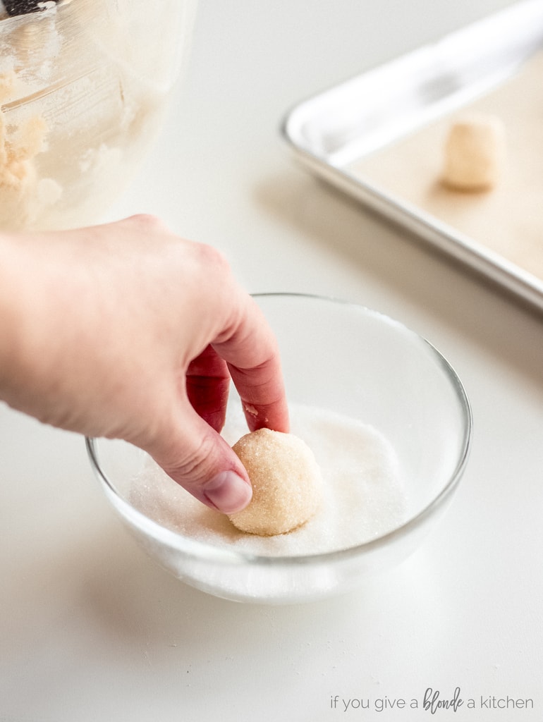 hand rolling ball of sugar cookie dough in granulated sugar
