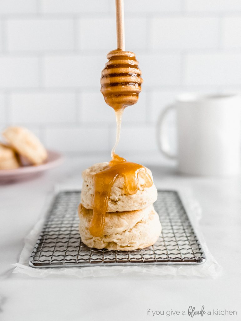honey dipper dripping honey over two buttermilk biscuits