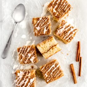 coffee cake square on parchment paper with vanilla glaze. Cinnamon stick and icing spoon