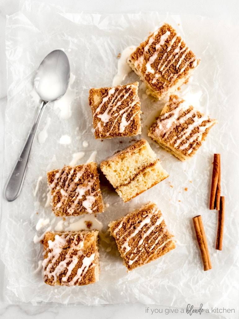 coffee cake square on parchment paper with vanilla glaze. Cinnamon stick and icing spoon