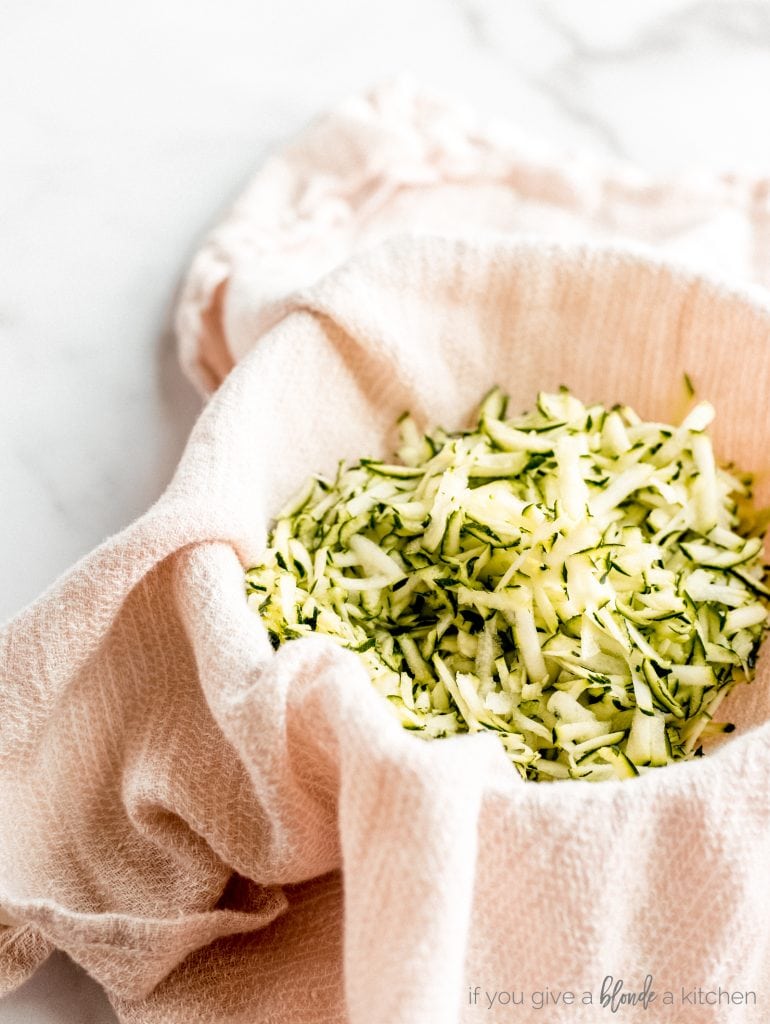 shredded zucchini on pink cloth draped over a bowl