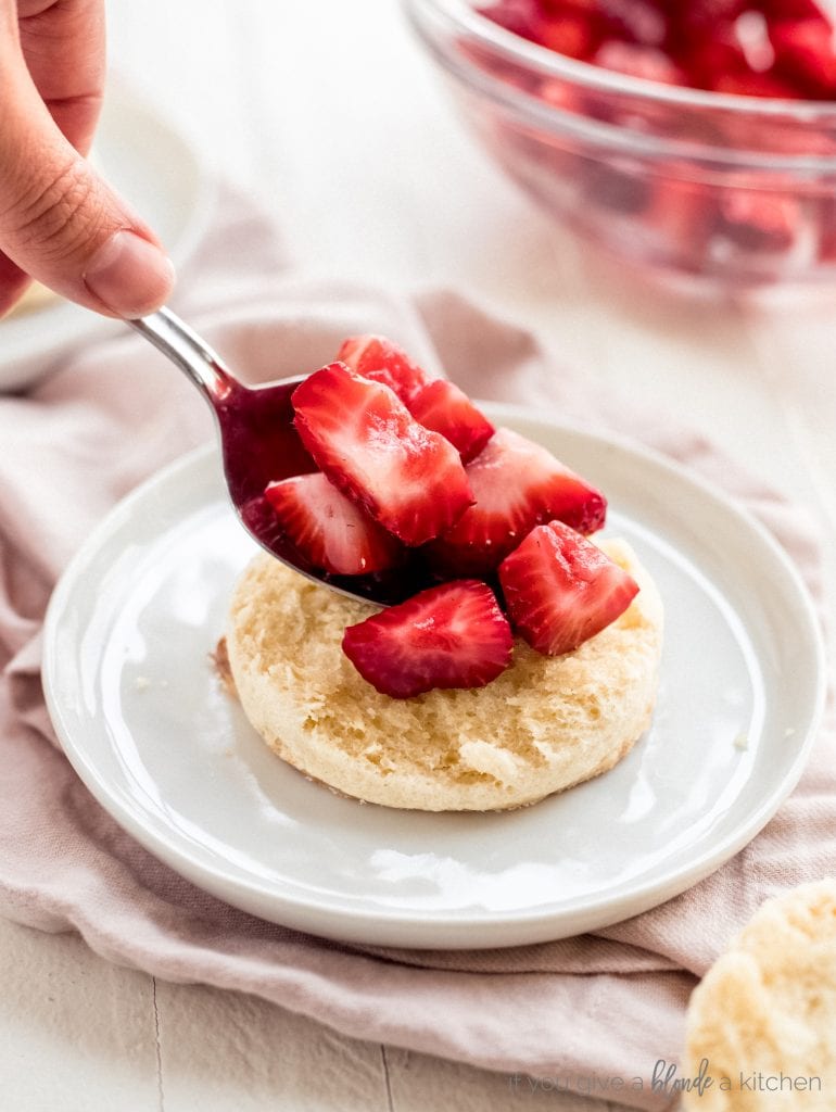 spoon placing strawberries on top of biscuit bottom