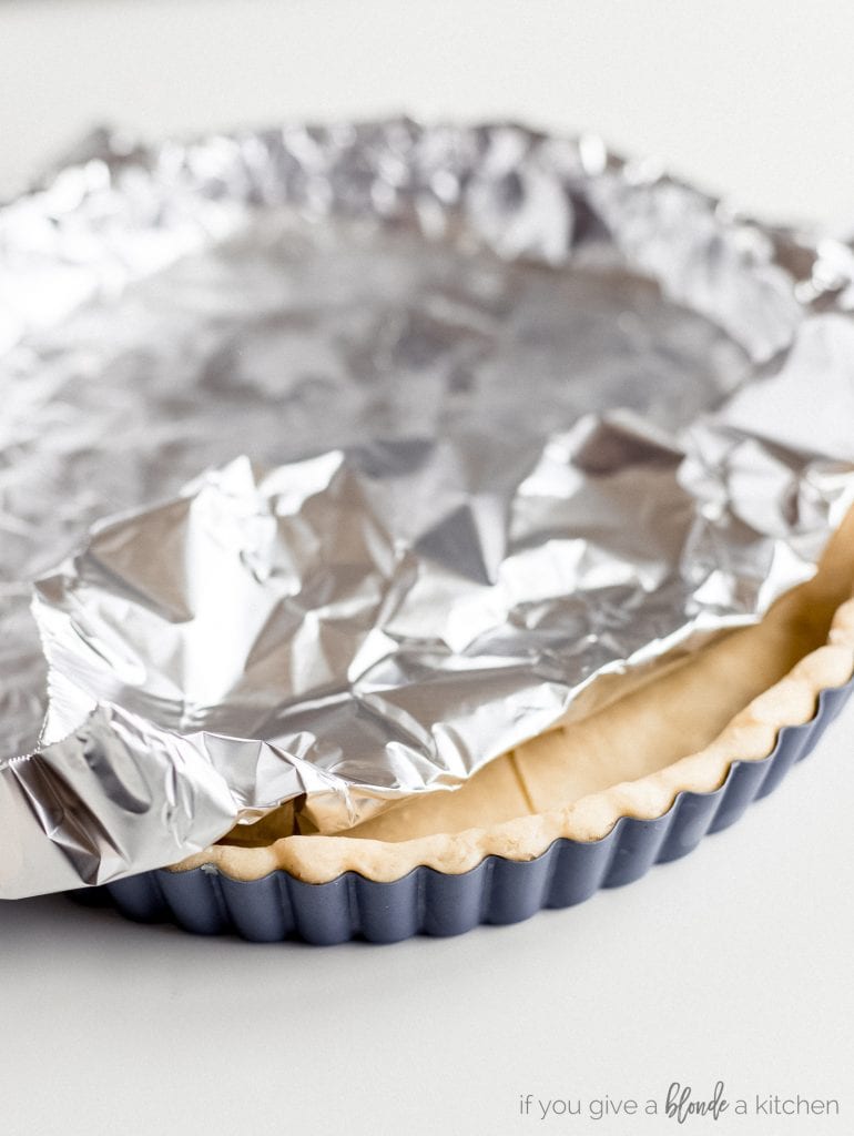 aluminum foil on top of tart pan with pastry dough