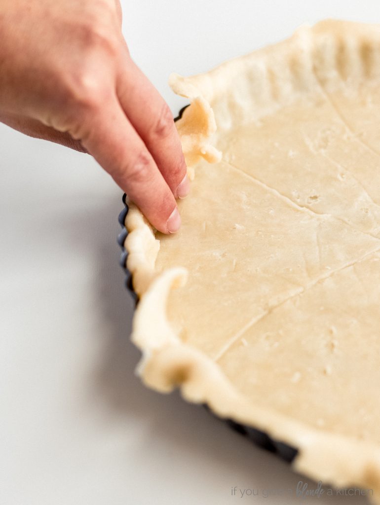 hand folding excess pastry dough inside the tart pan