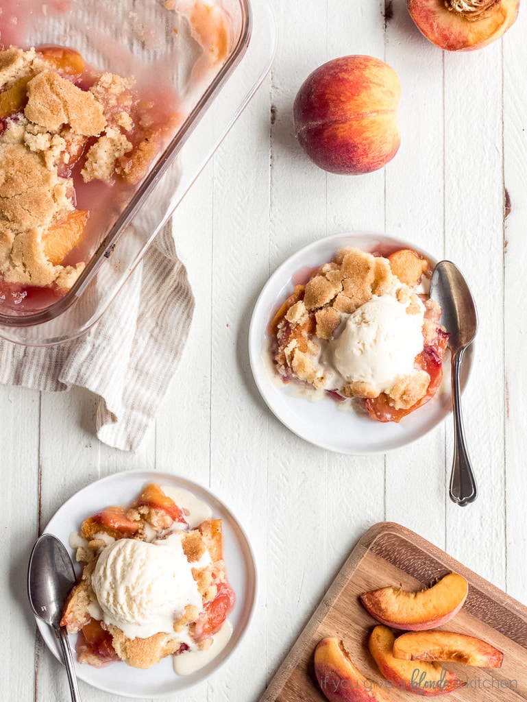 two round plates with peach cobbler and scoop of vanilla ice cream; small cutting board with peach slices; baking dish with peach cobbler
