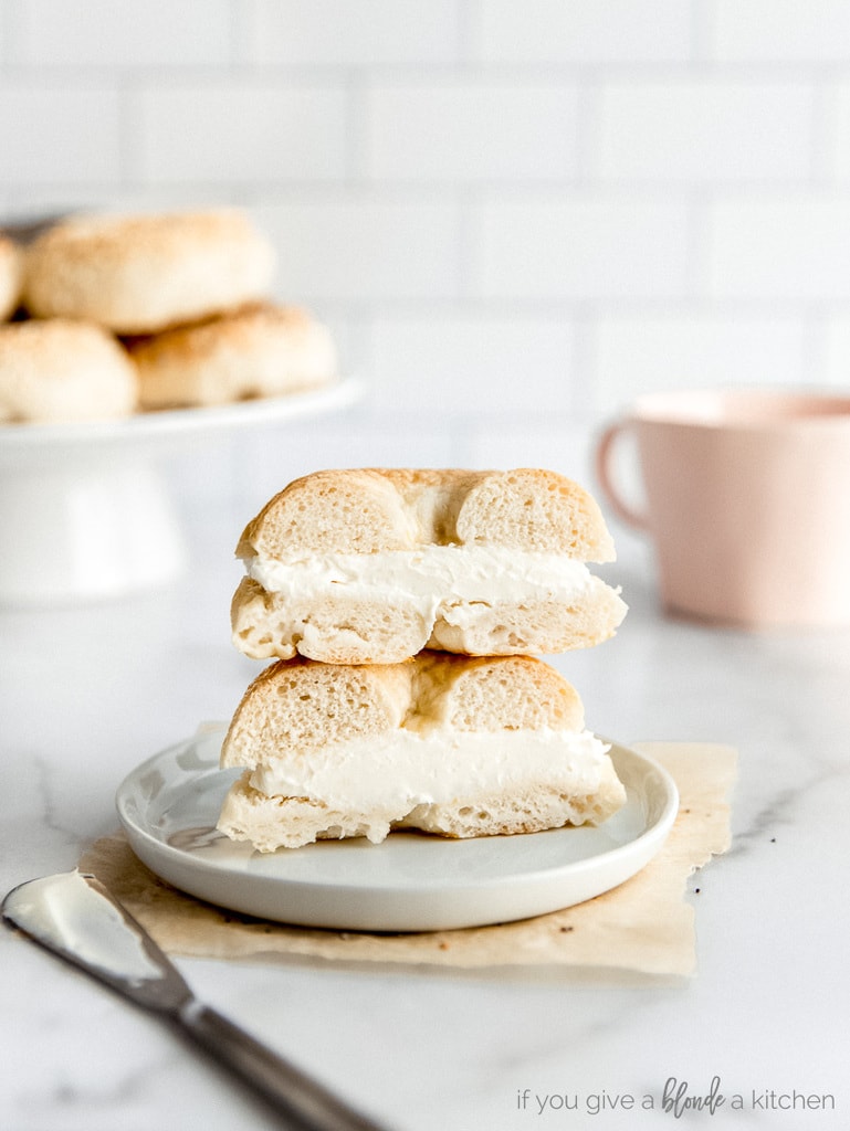 homemade plain bagel cut in half with cream cheese; halves stacked on top of each other on small white plate