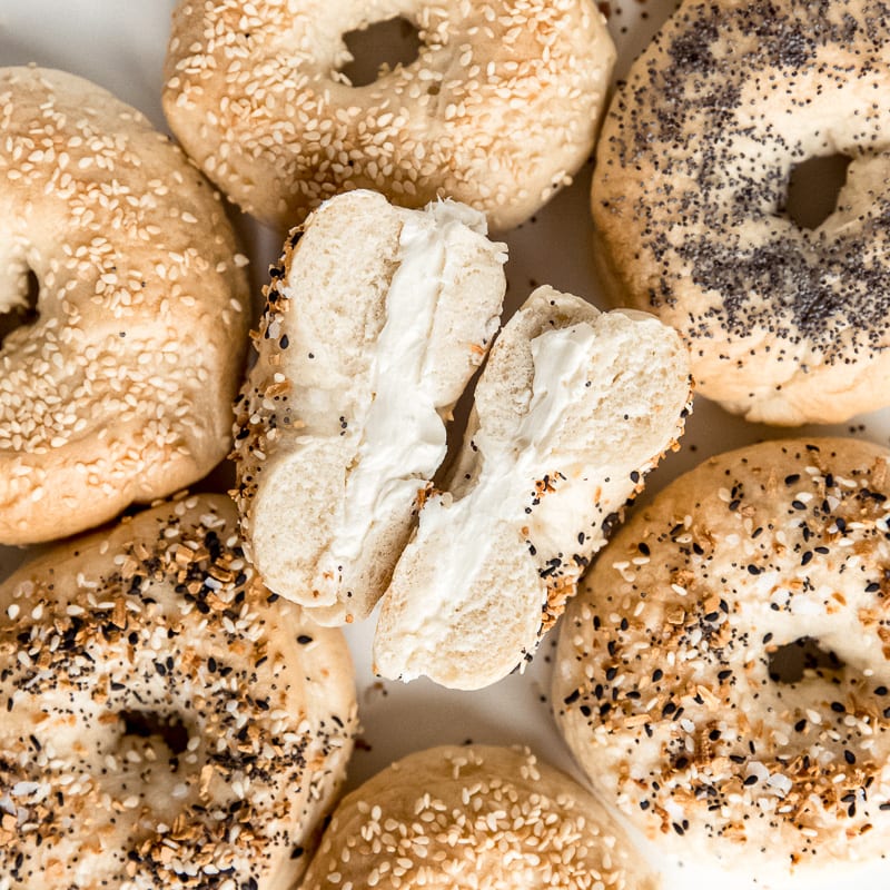 bagel with cream cheese cut in half showing inside; surrounded by bagels