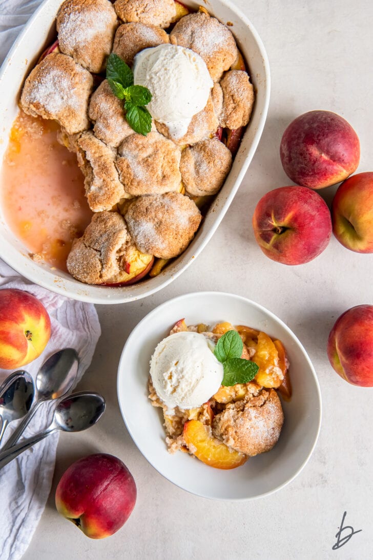 peach cobbler in a baking dish next to bowl of peach cobbler served with scoop of vanilla ice cream