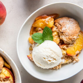 peach cobbler in a bowl with scoop of vanilla ice cream and sprig of mint leaves