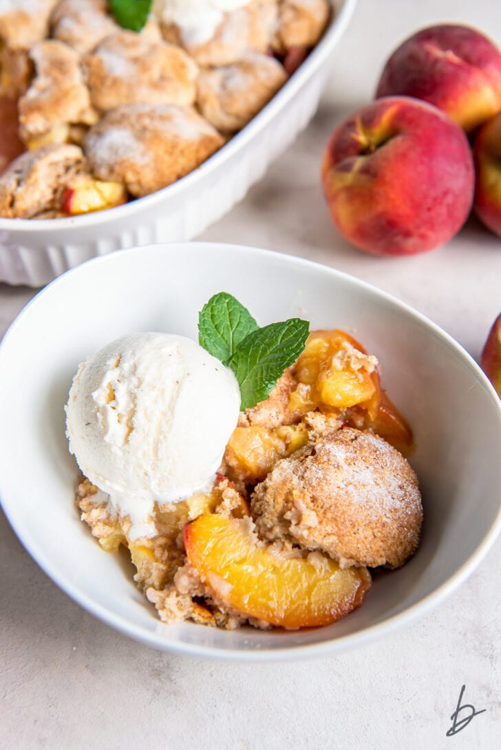 peach cobbler servings in a bowl topped with a scoop of vanilla ice cream and sprig of mint