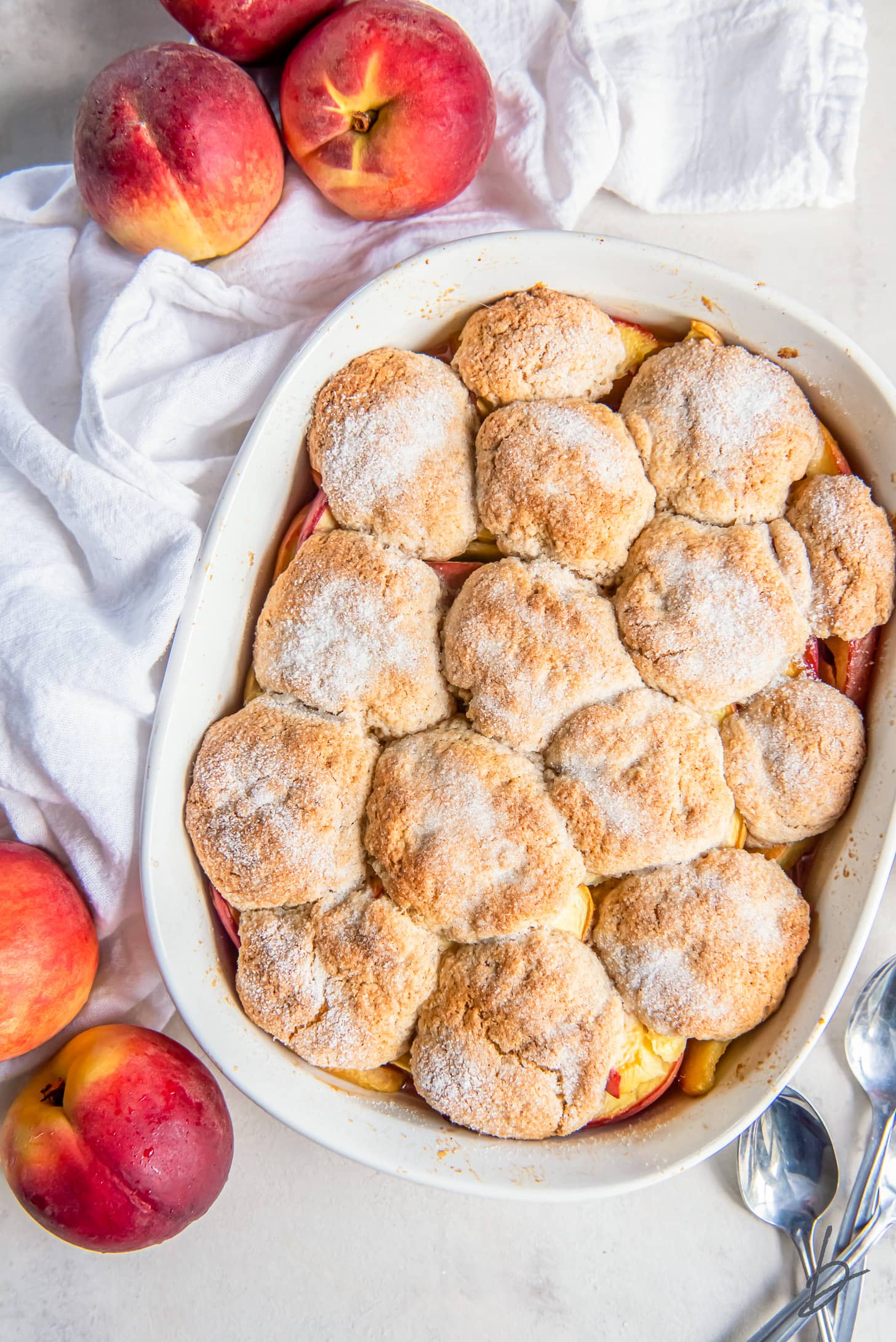 homemade peach cobbler in a baking dish with sugar sprinkled on top of baked biscuit topping
